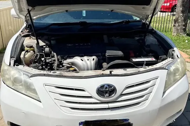 White Toyota Camry with the bonnet up and the engine bay open on a paved driveway